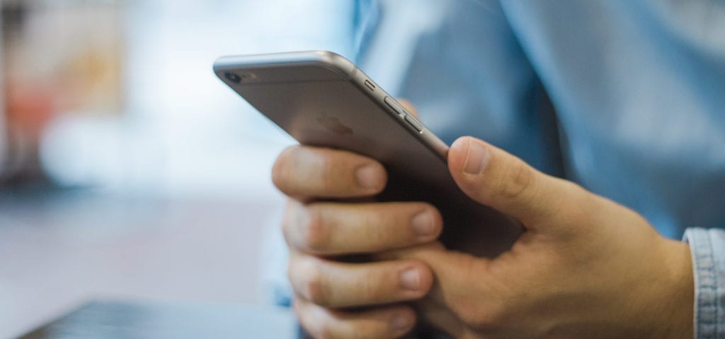 A man wearing a blue shirt holds a silver iPhone in front of him.