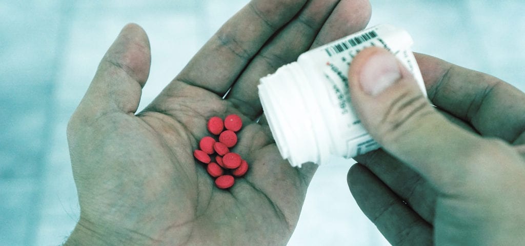 A man dumps red-colored pharmaceuticals into the palm of his hand.