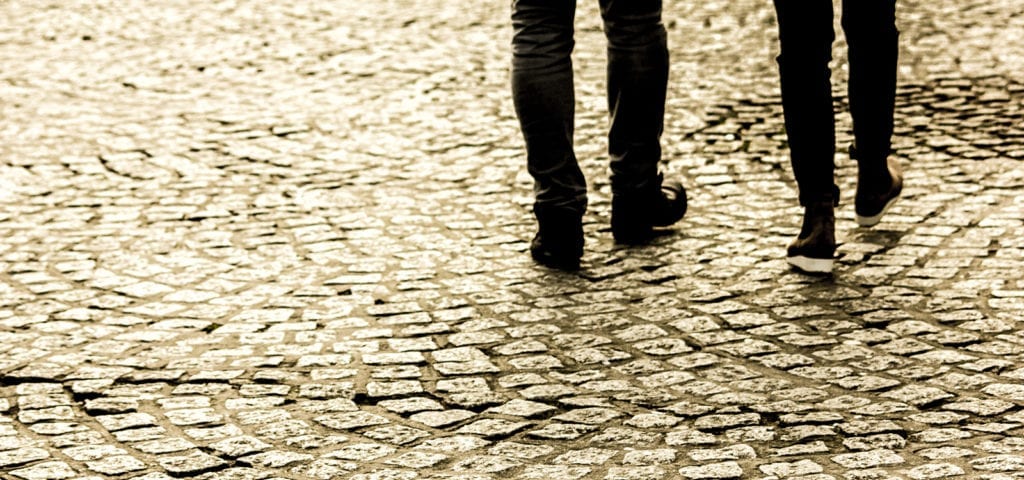 Two individuals walking on a cobblestone street.