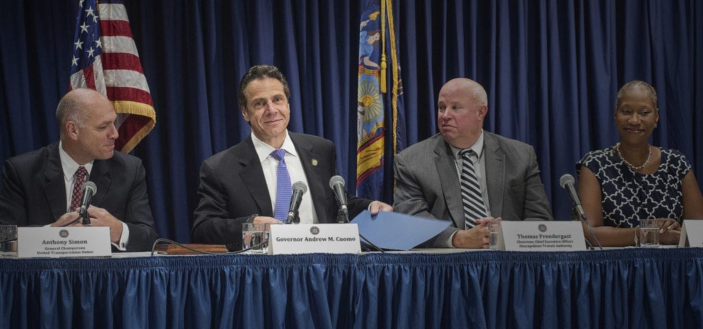 New York Gov. Andrew Cuomo sits at a table of speakers at a community event.