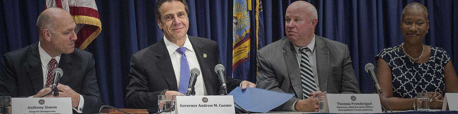 New York Gov. Andrew Cuomo sits at a table of speakers at a community event.
