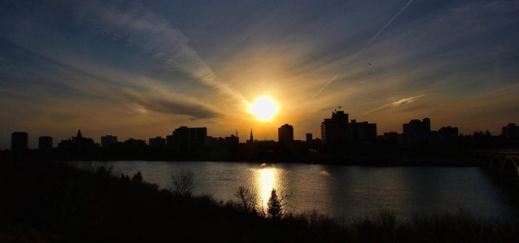 The city skyline of Saskatoon, Saskatchewan silhouetted by a setting sun.