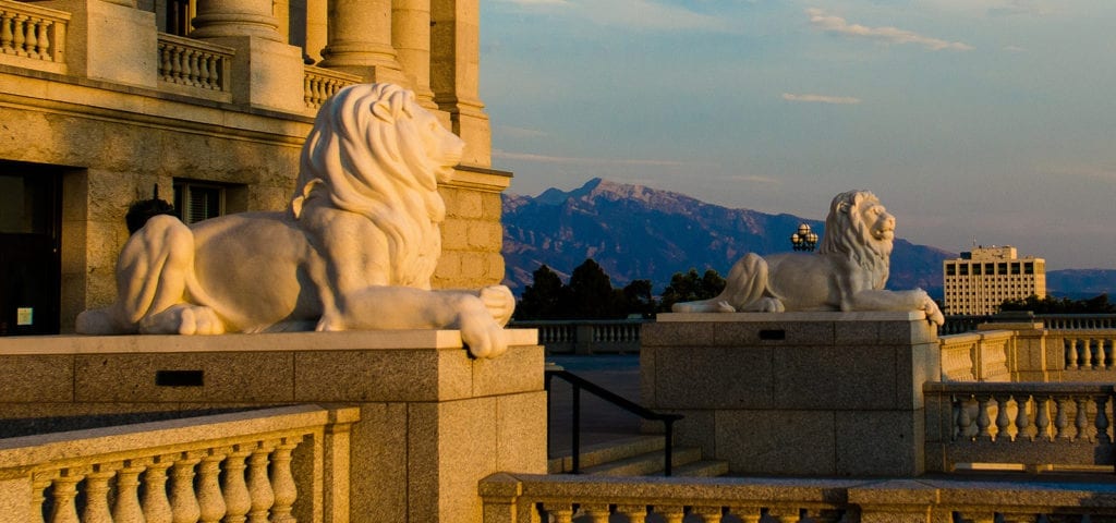 Two lion statues rest on either side of a marble stairway leading up to the Utah State Capitol Building in Salt Lake City, Utah.