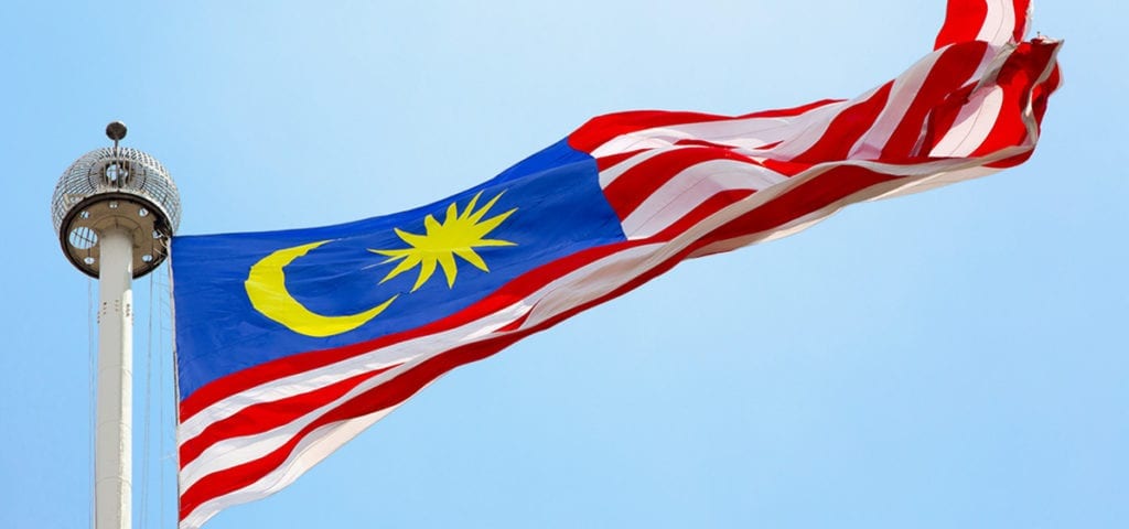 The flag of Malaysia flies on a clear, blue sky day.