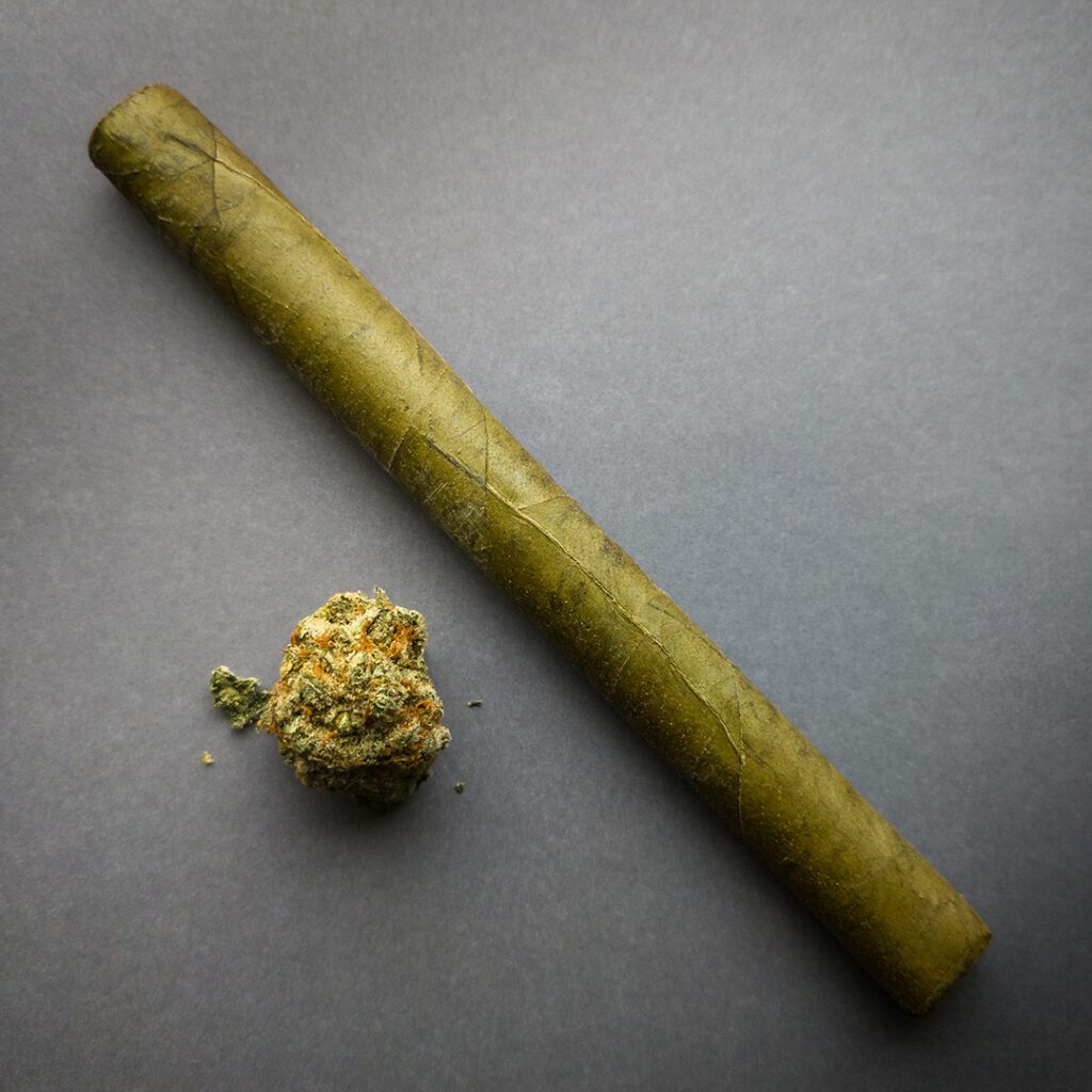 a natural cannagar rolled with cannabis leaves next to a nug